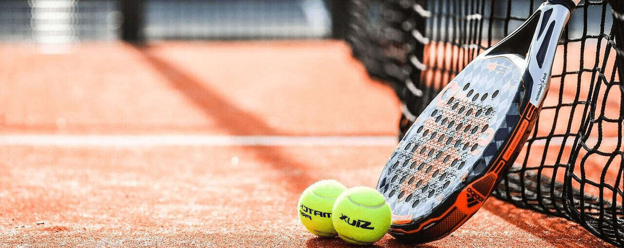 One pickleball paddle and two tennis balls on an orange carpeted court